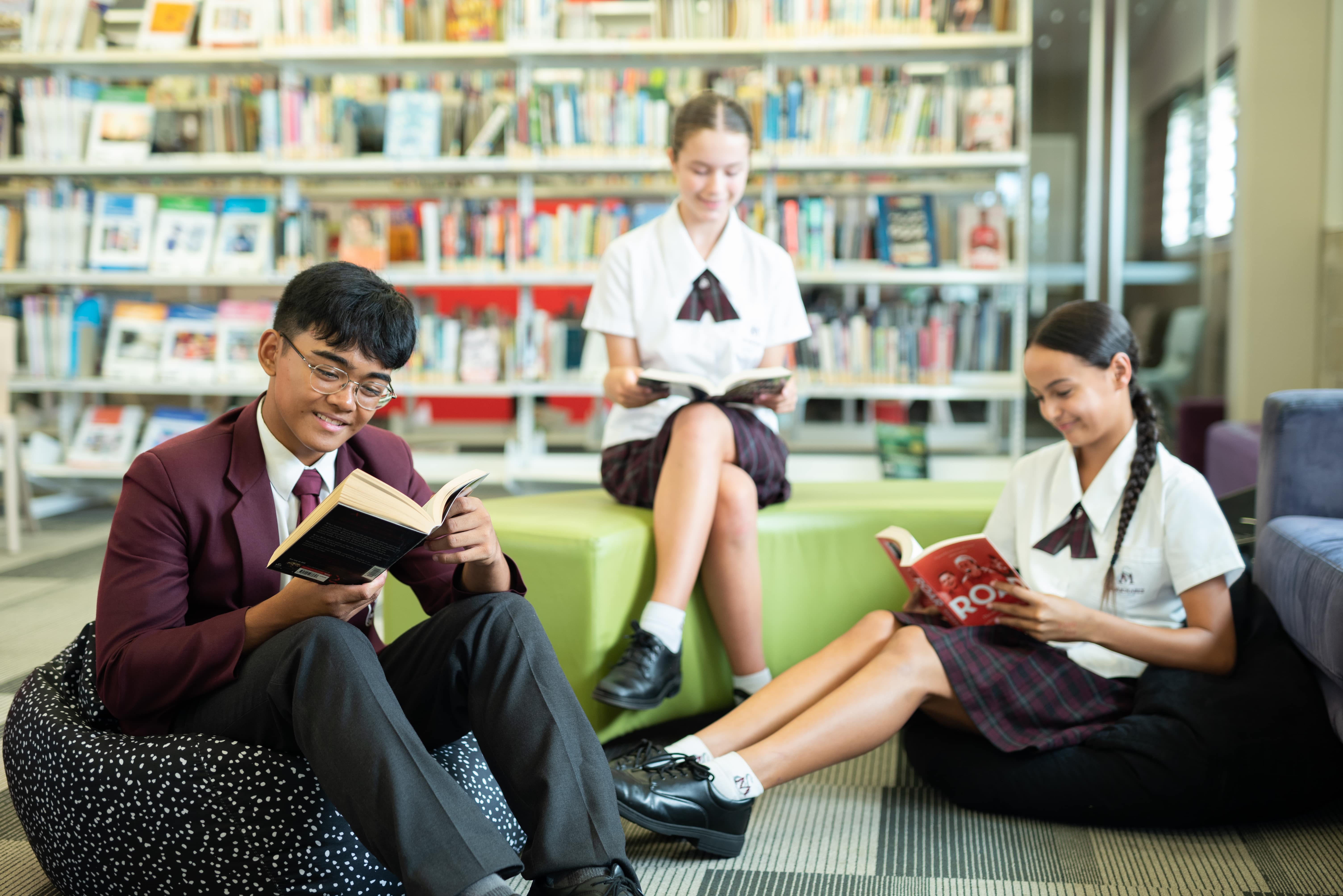 Students reading books independently in a school library, seated on soft furniture in a quiet learning space