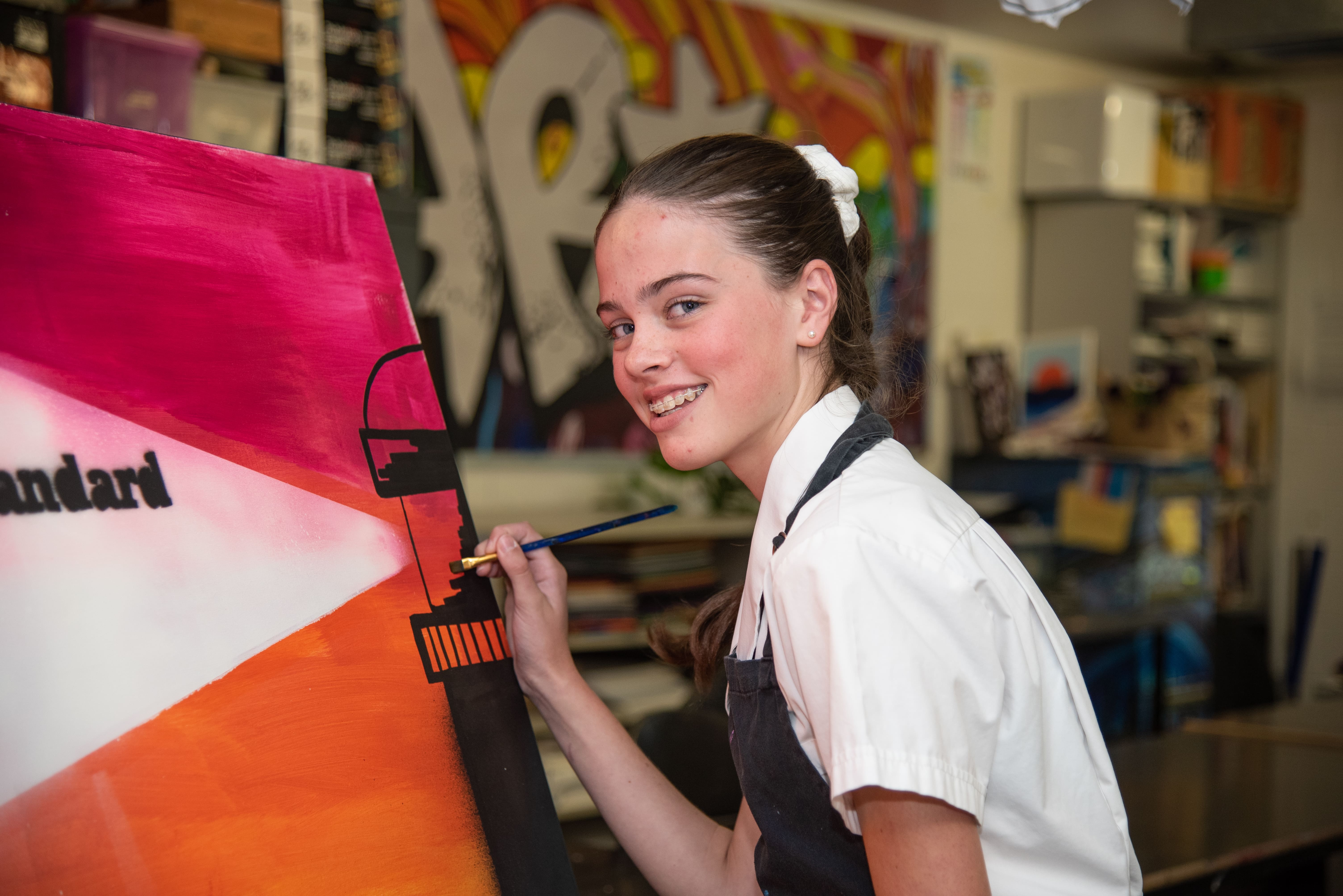 Student painting on a large canvas in an art classroom with colourful mural behind