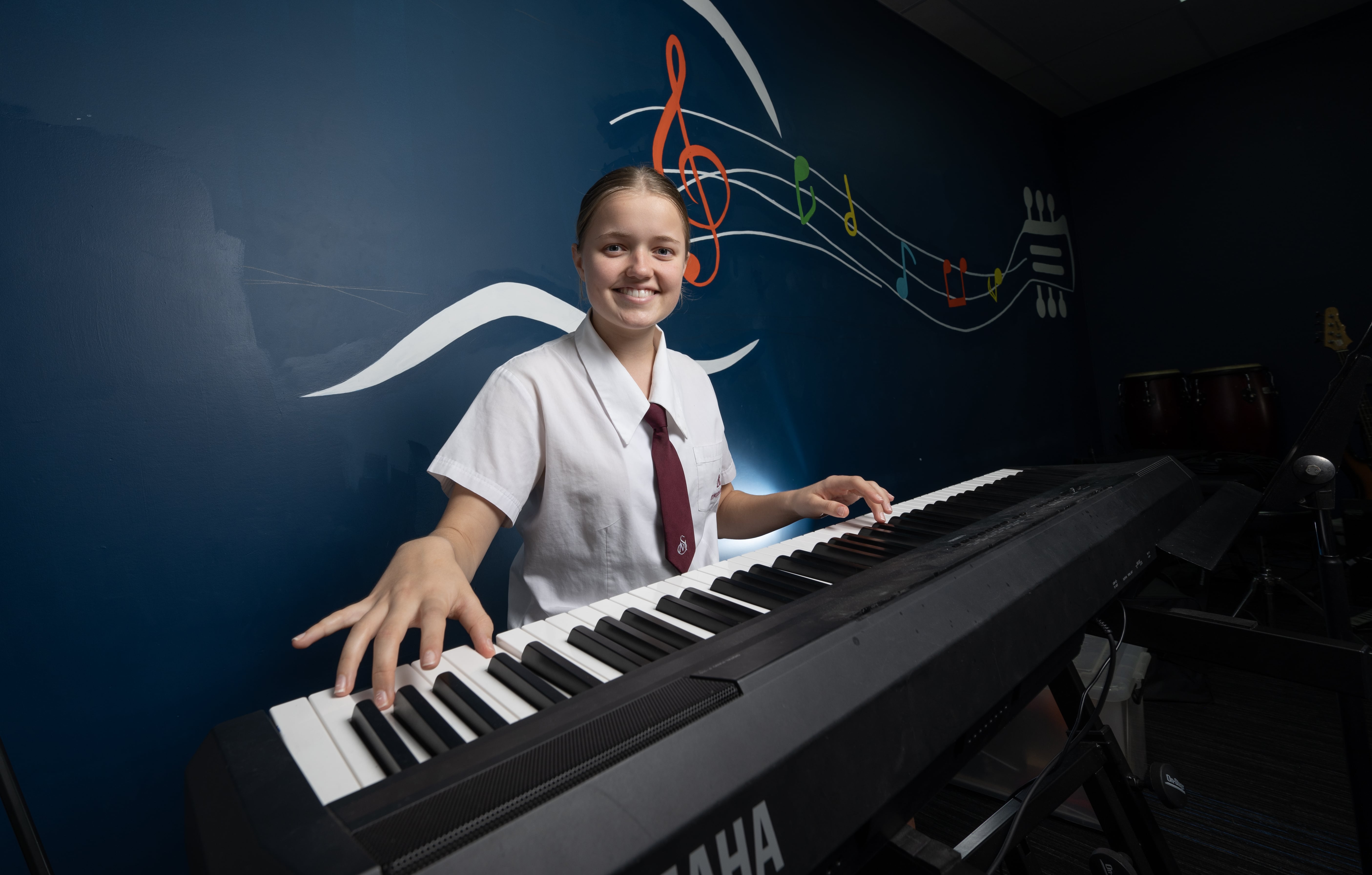 Student playing keyboard in a music room with wall art featuring musical notes