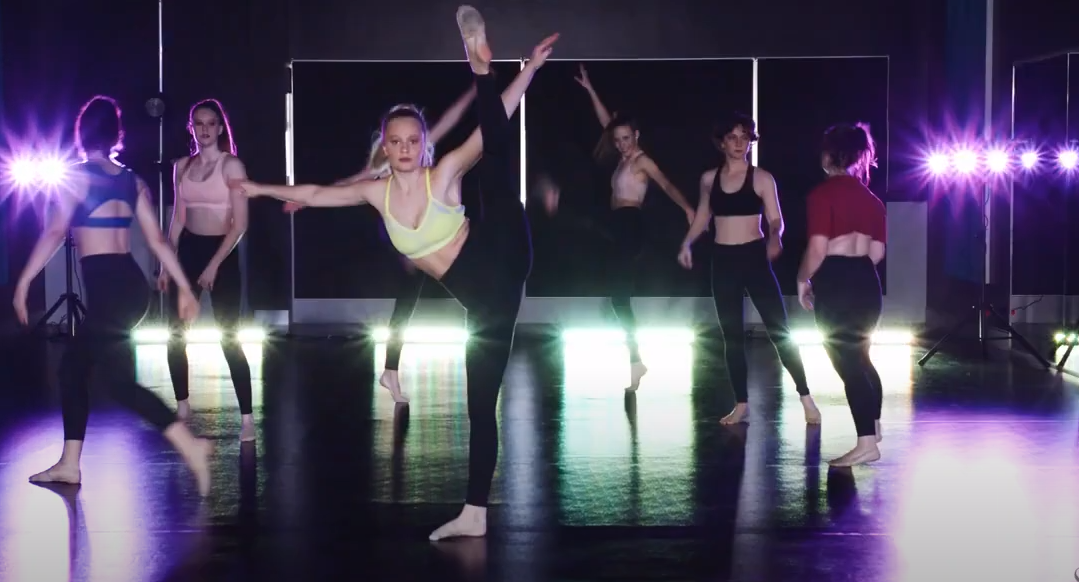 Students rehearsing a contemporary dance routine in a studio with stage lighting and mirrors