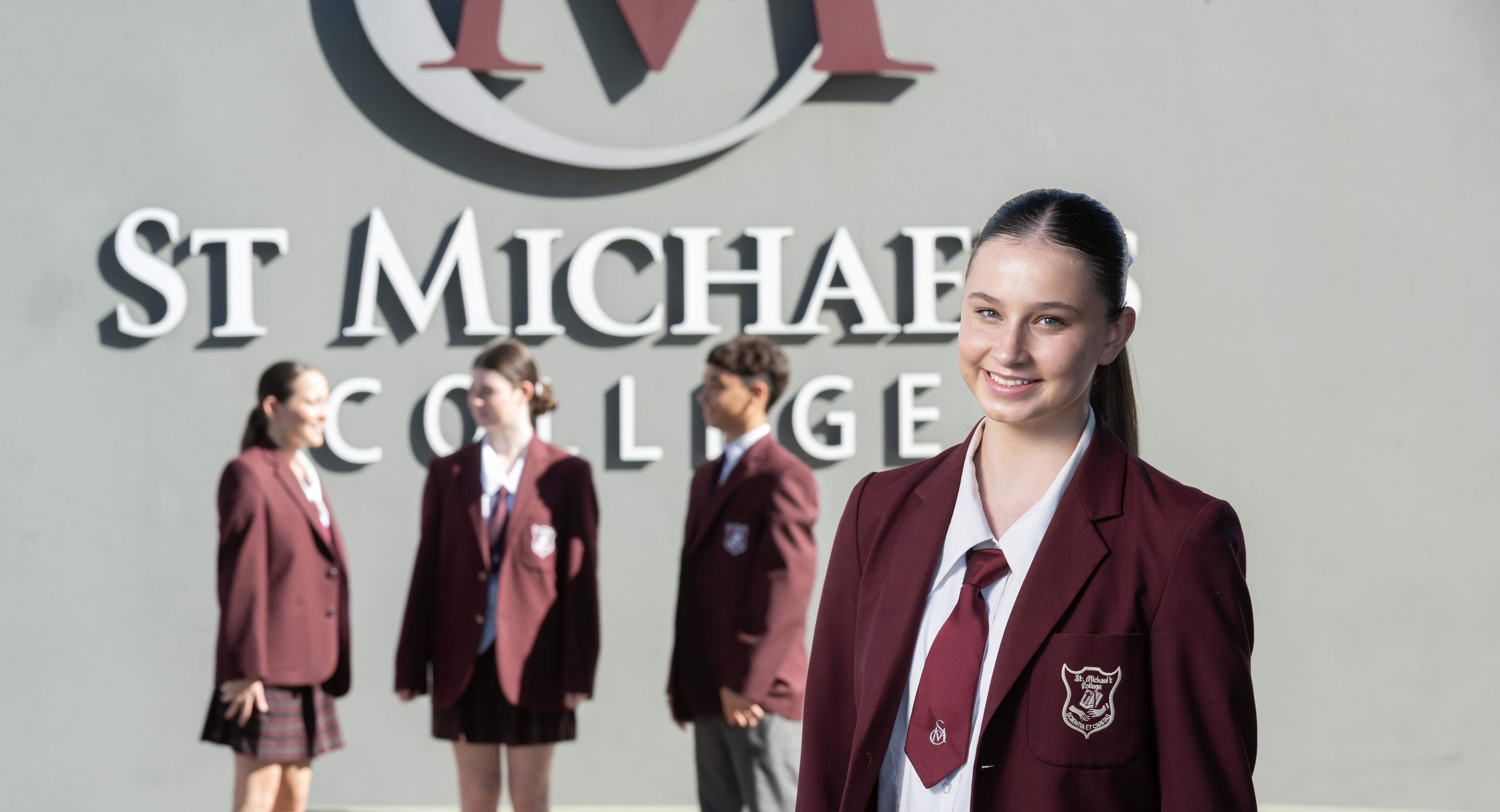 Student in school uniform standing in front of St Michael’s College signage, with other students blurred in the background