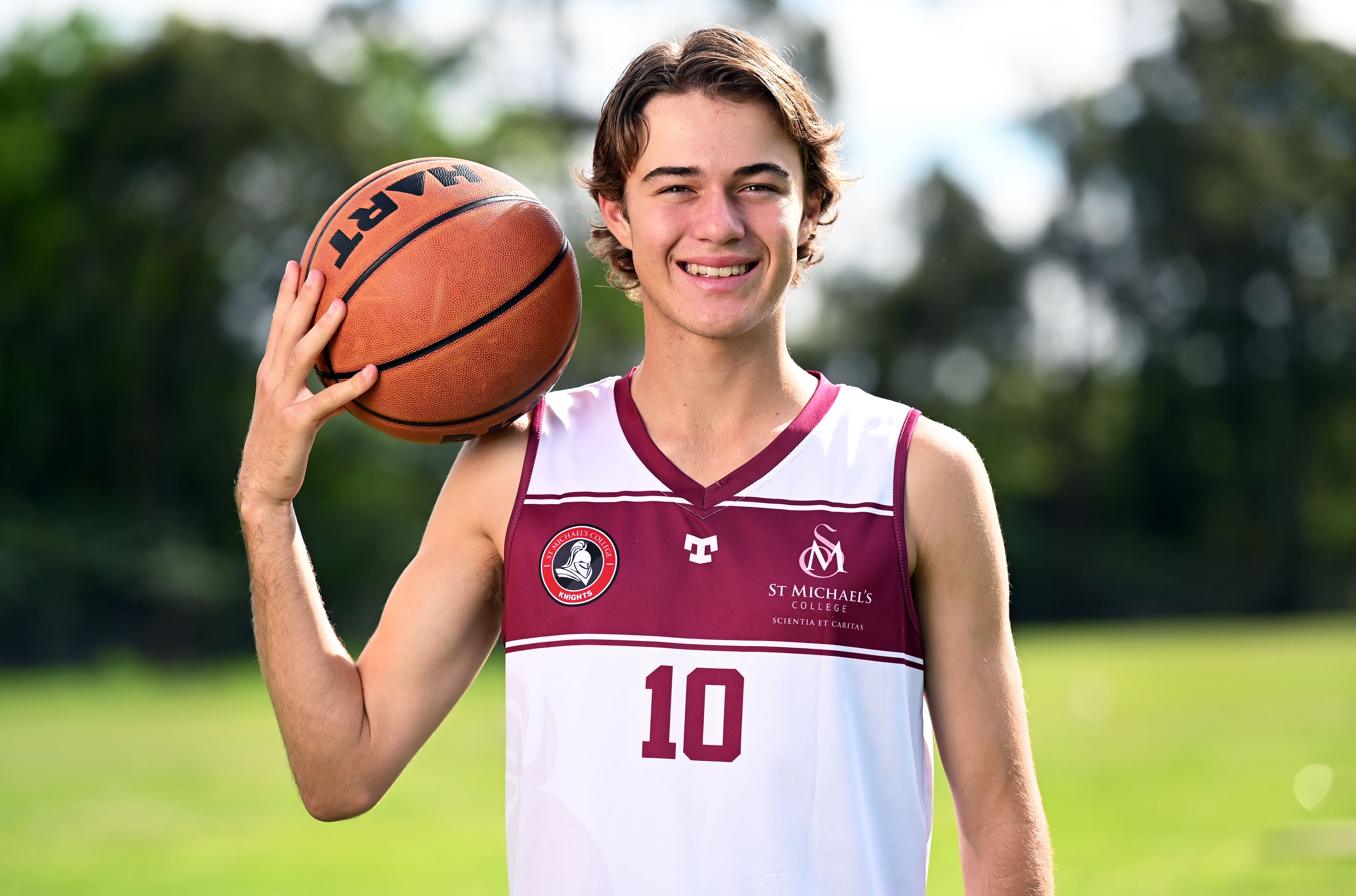 Student holding a basketball on a field in school sports uniform during an individual sports portrait