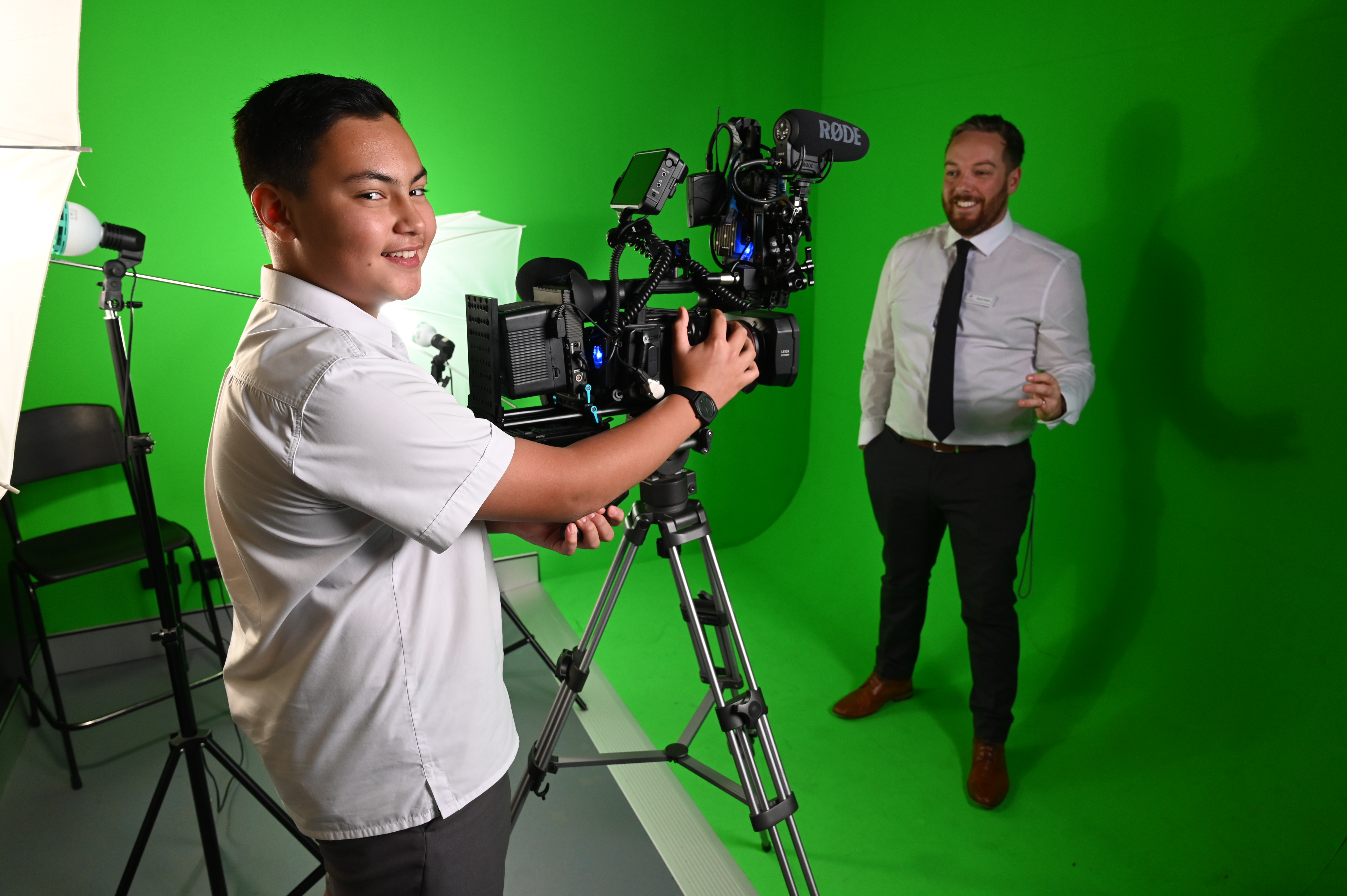 Student operating a professional video camera in a green screen studio while filming a staff member presenting