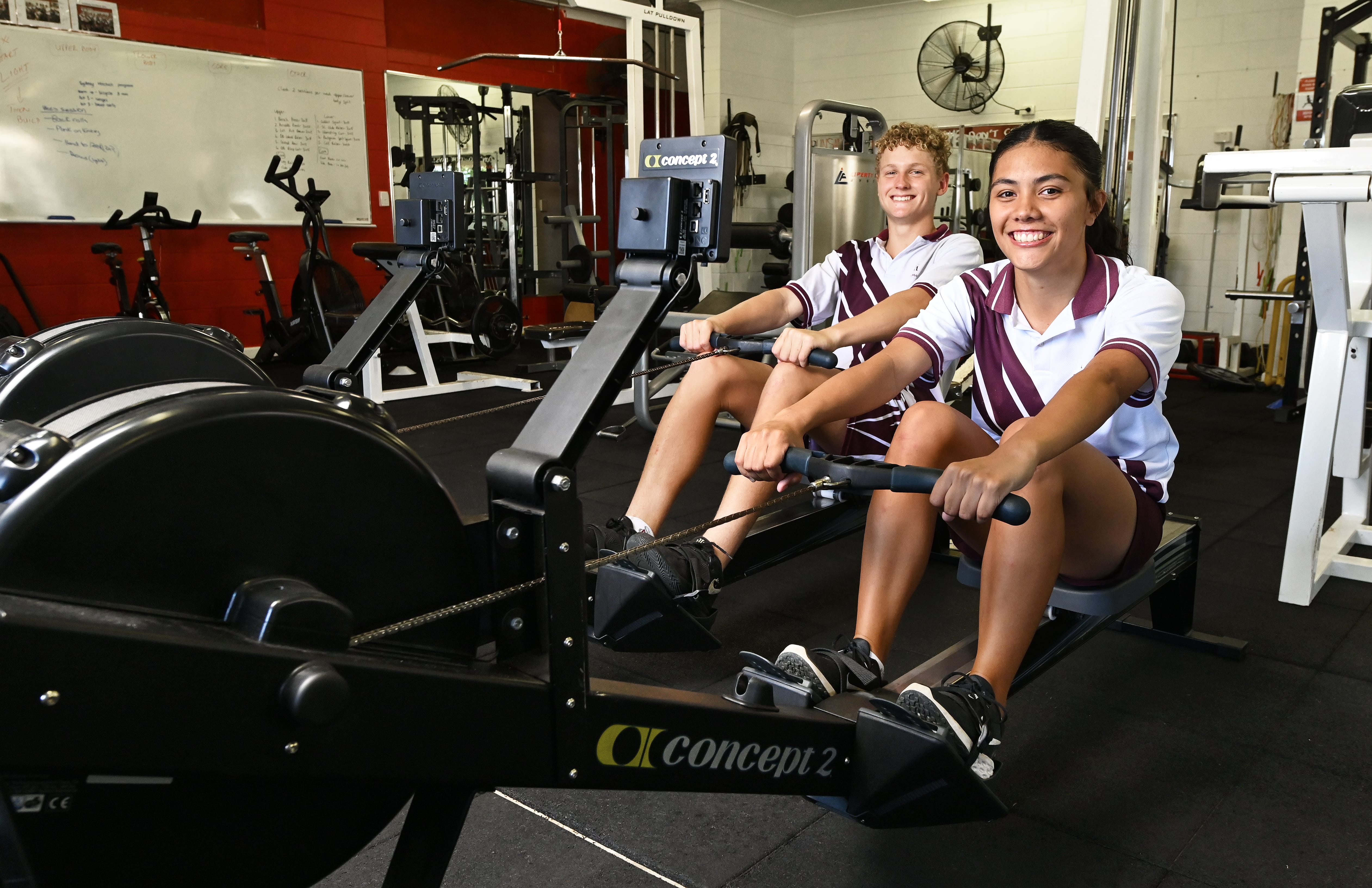 Students in school uniform using rowing machines in a gym during a fitness training session