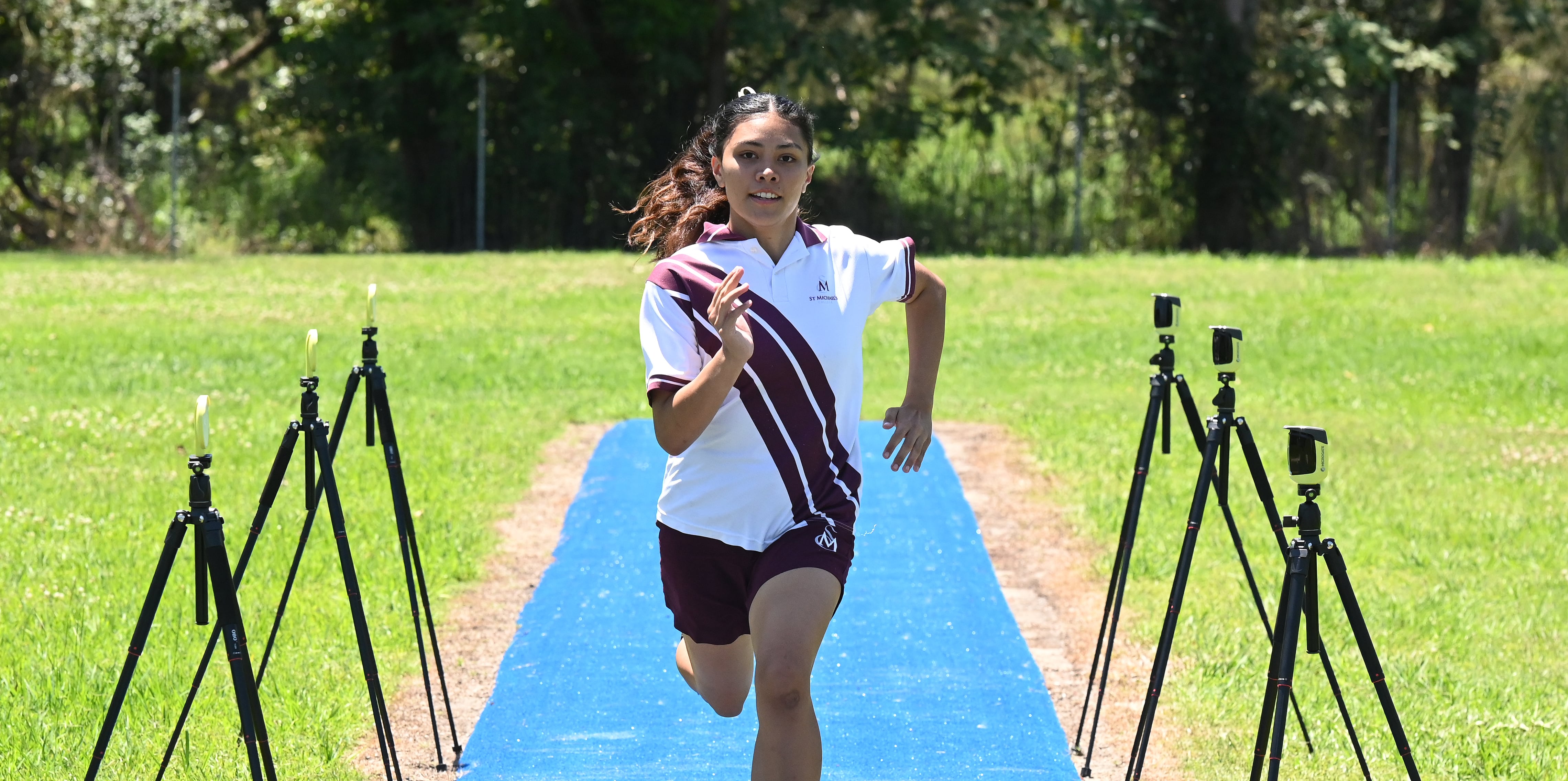 Student running along an athletics track between timing sensors during a sprint training activity
