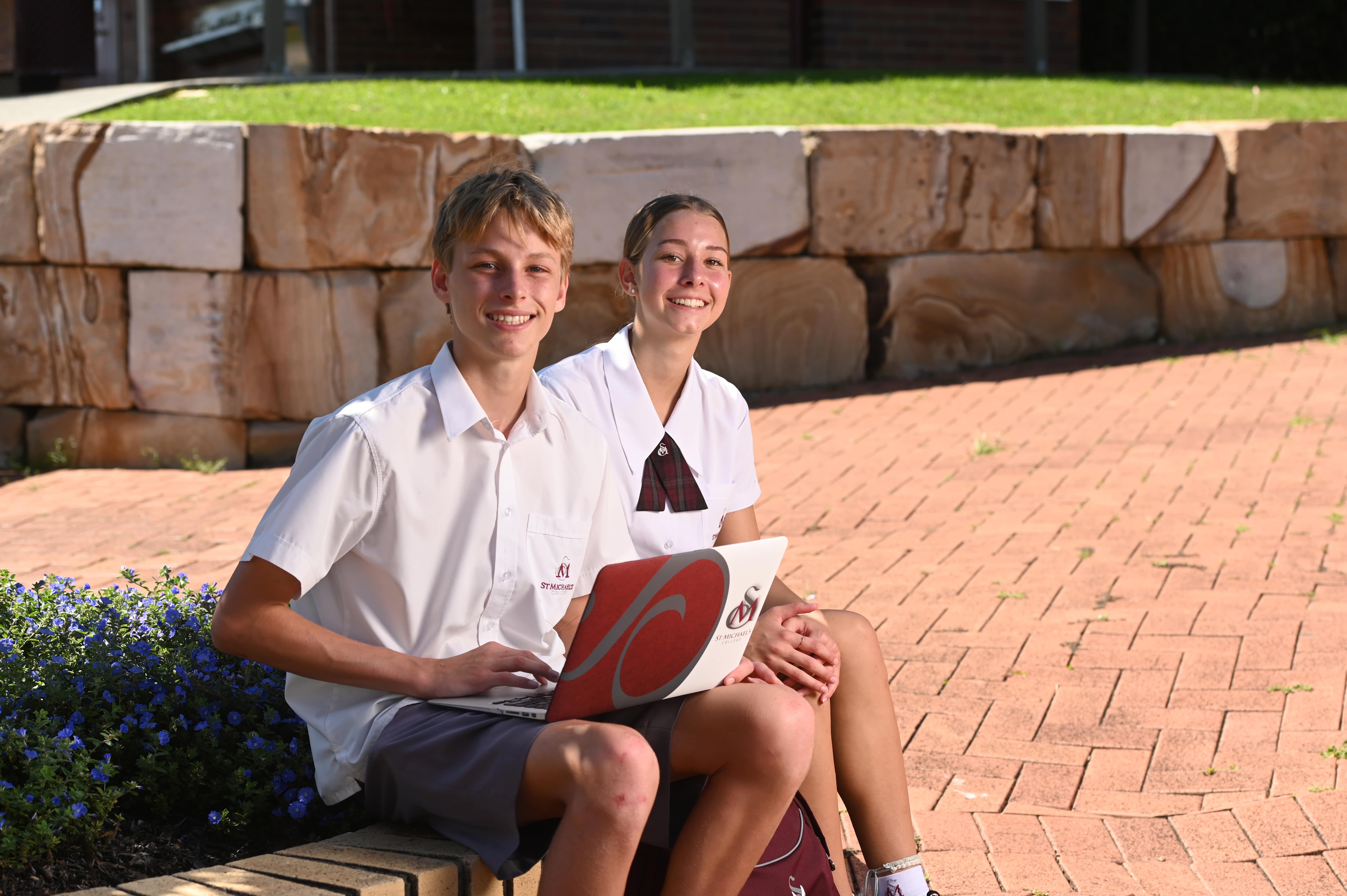 Students sitting outdoors in a school courtyard using a laptop and working together in a collaborative learning setting