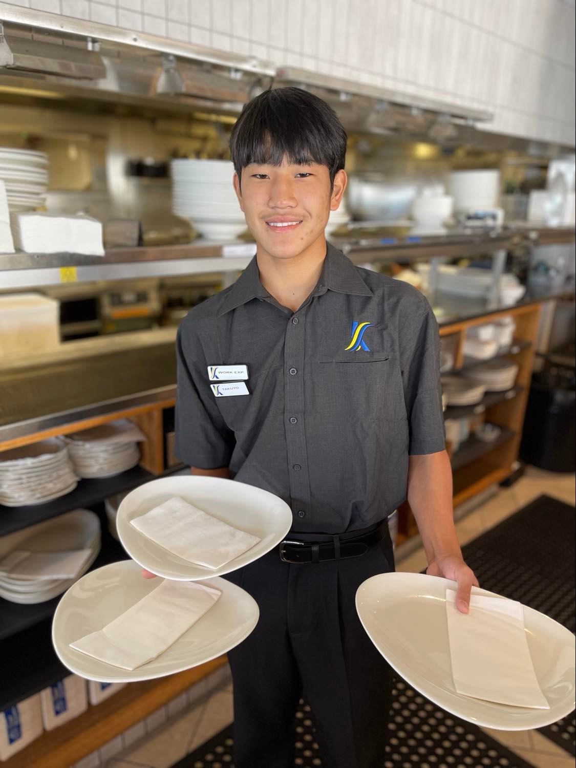 Student in hospitality uniform holding plates in a commercial kitchen during a food service activity
