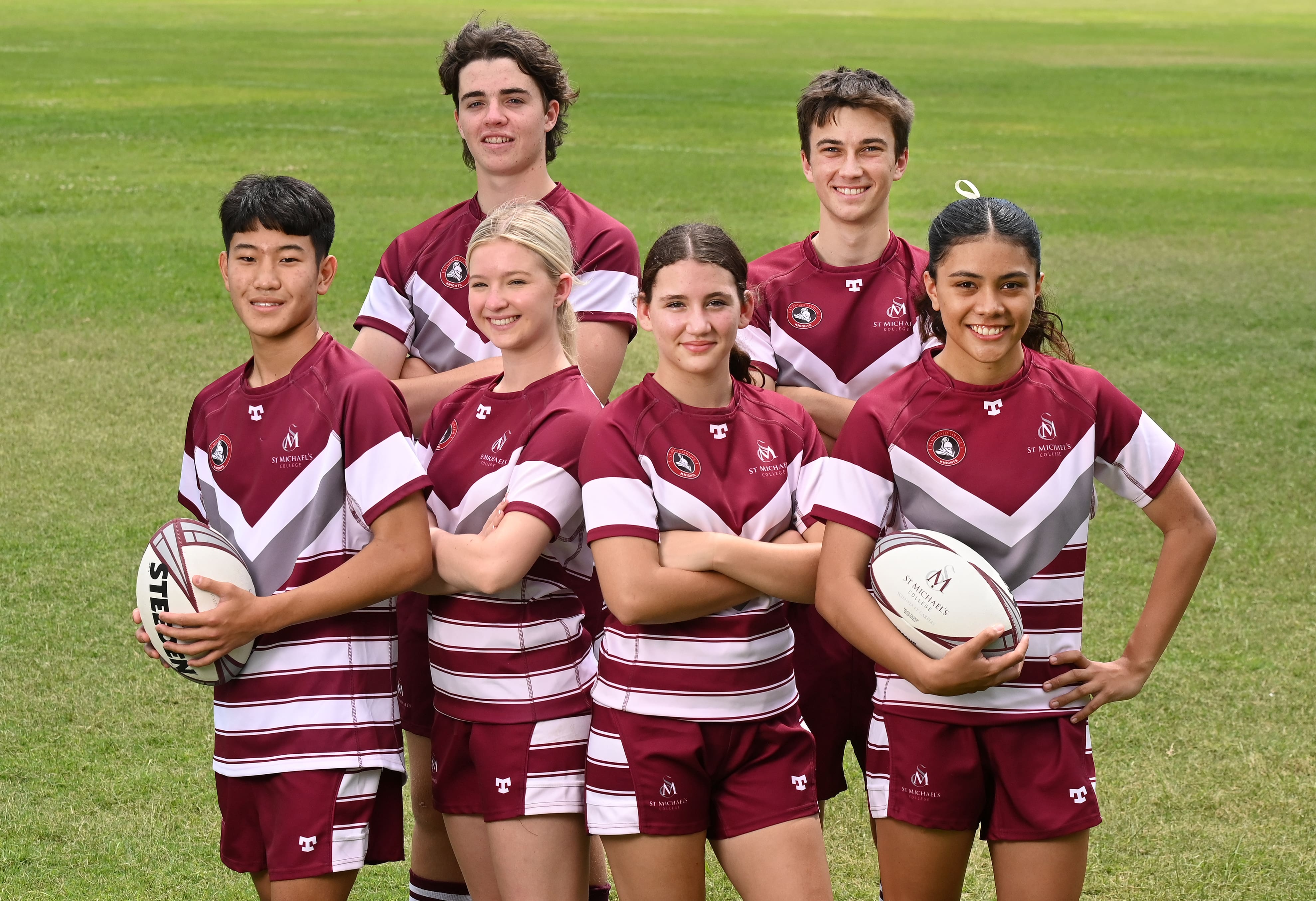Students standing together on a field in sports uniforms holding rugby balls during a team photo